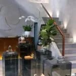 Maliit na larawan: mga eskaparateng salamin, isang halamang nakapaso at hagdanang may barandilyang kahoy sa loob ng showroom ng R Parfums