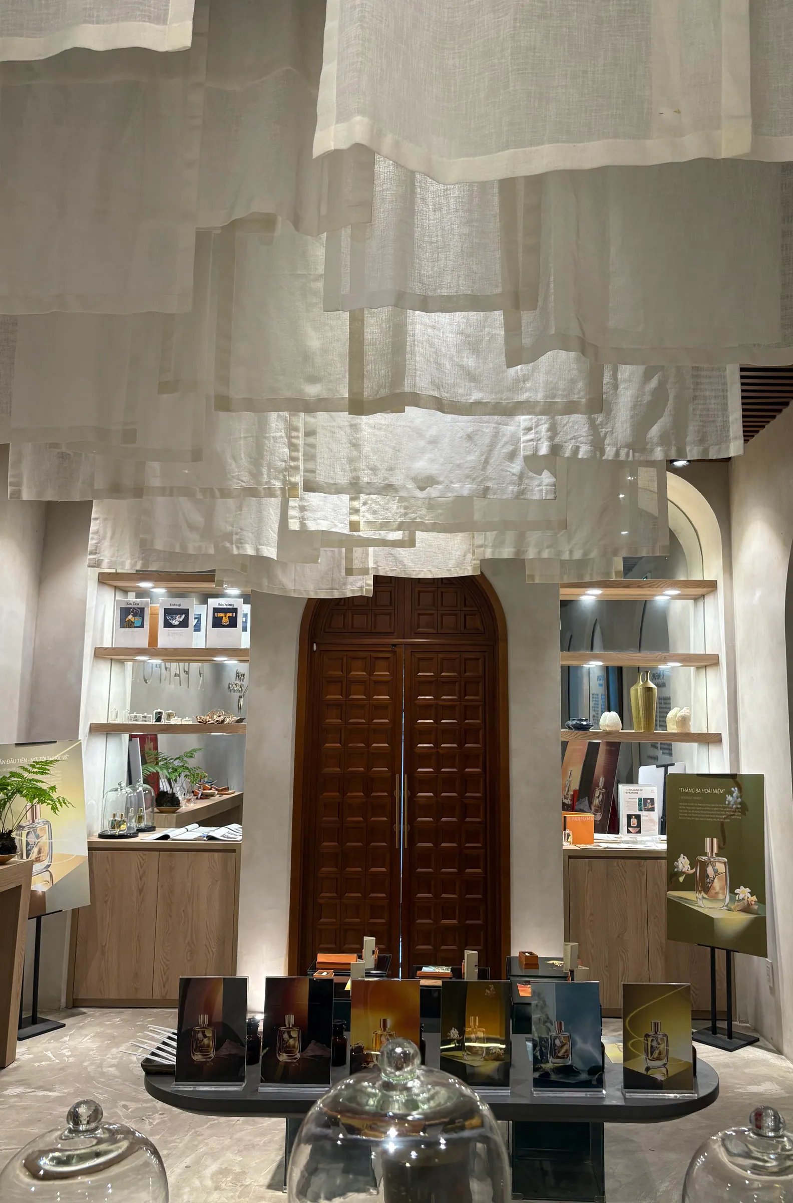 Panel linen tergantung rendah dari siling di hadapan pintu kembar kayu yang tinggi, berpanel segi empat dan melengkung di bahagian atas; rak kayu bercahaya di kedua-dua sisi, sebuah meja pameran rendah di hadapan