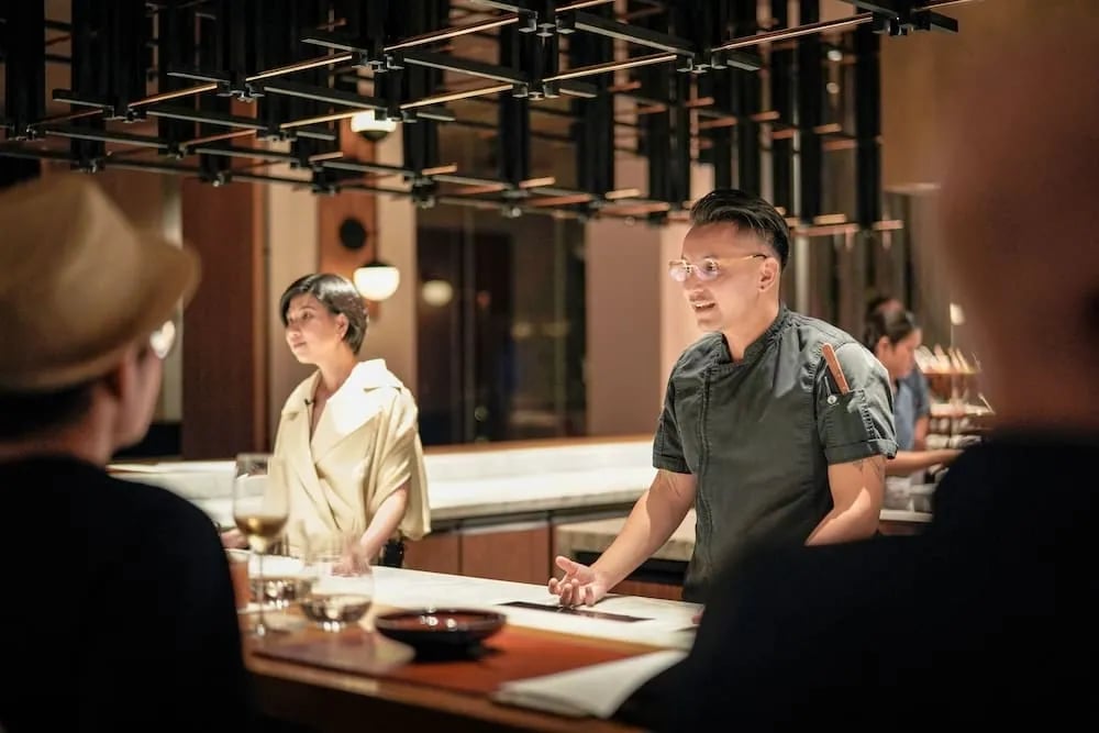 Sina Rei Nguyen at Chef Andy Huynh sa likod ng isang counter na marmol, nakikipag-usap sa mga panauhin sa restawrang Oku