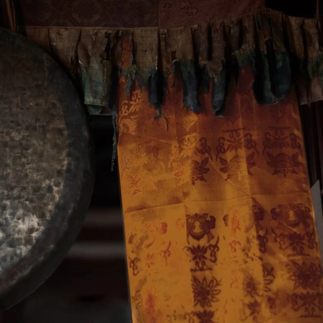 Sedang kulay-luyang-dilaw na may limbag na lumang disenyo sa ilalim ng gutay-gutay at punit na gilid ng tela, sa tabi ng isang madilim na gong na tanso sa mahinang ilaw