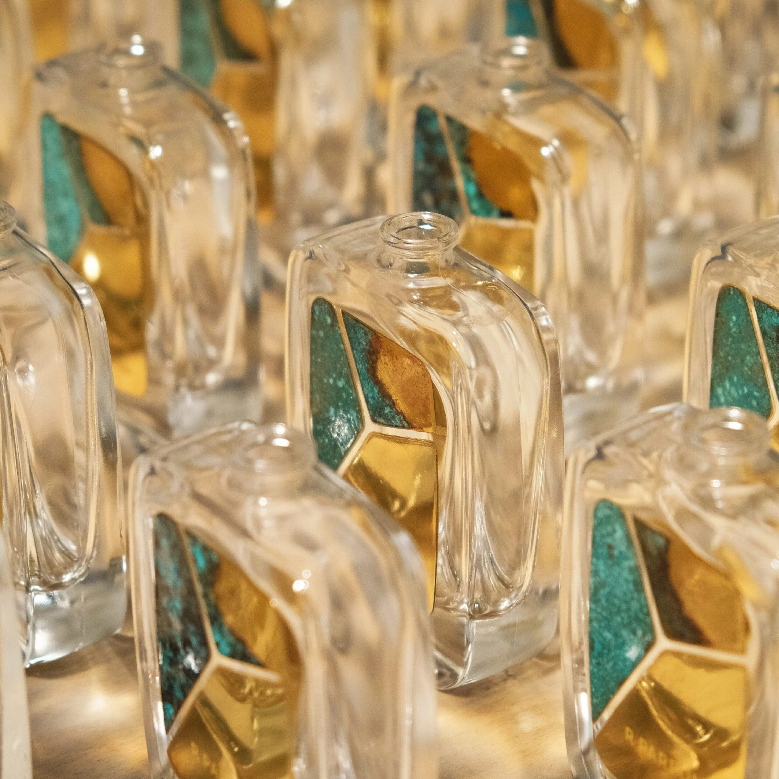 Deretan botol kaca R Parfums berkepingan loyang berpatina hijau dan emas, setiap satu dengan corak berbeza