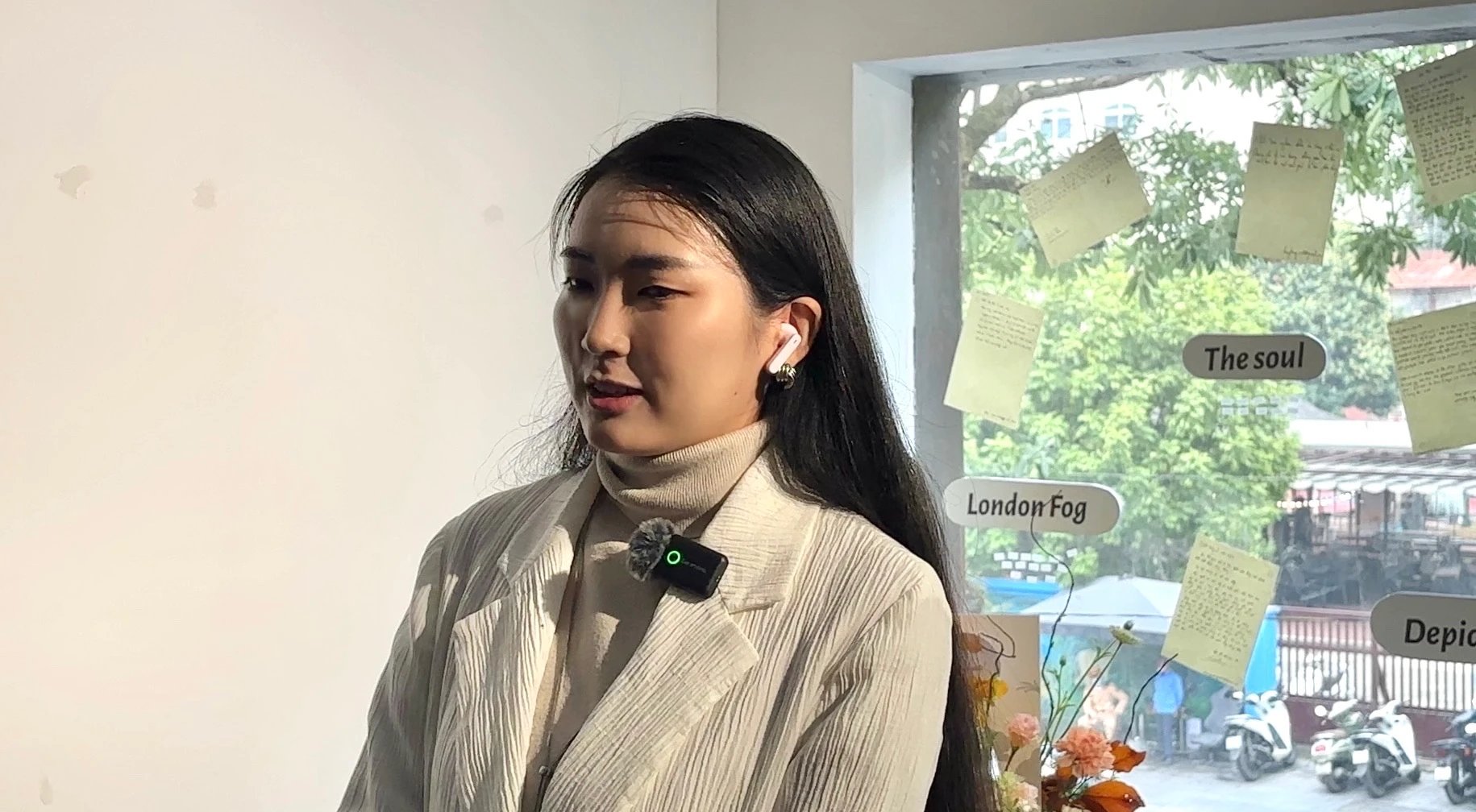 ผู้เข้าชมหญิงติดไมโครโฟนหนีบปกเสื้อเล่าความประทับใจ ข้างแผงกระจกที่มีจดหมายลายมือและป้าย ‘London Fog, The soul’