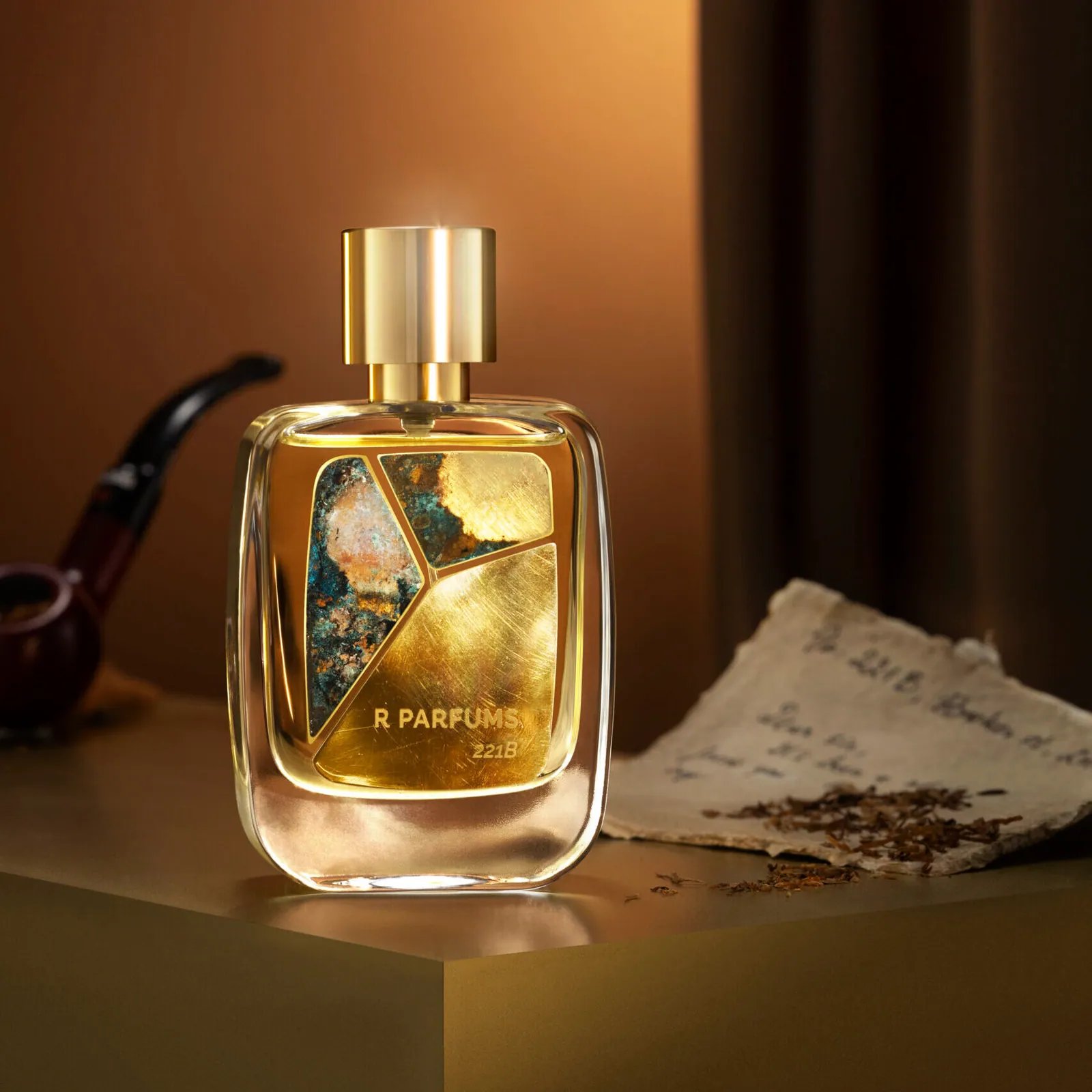 Botol 221B oleh R Parfums dengan kepingan loyang berpatina, di sisi sebatang paip rokok, tembakau lerai dan sepucuk surat lama dalam cahaya keemasan yang hangat