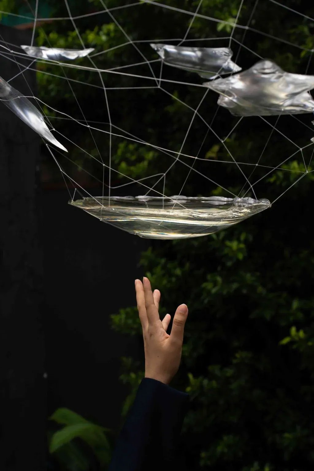 Sebelah tangan menjangkau ke atas di bawah jaring tali halus yang memegang kepingan resin jernih, seperti lopak air hujan