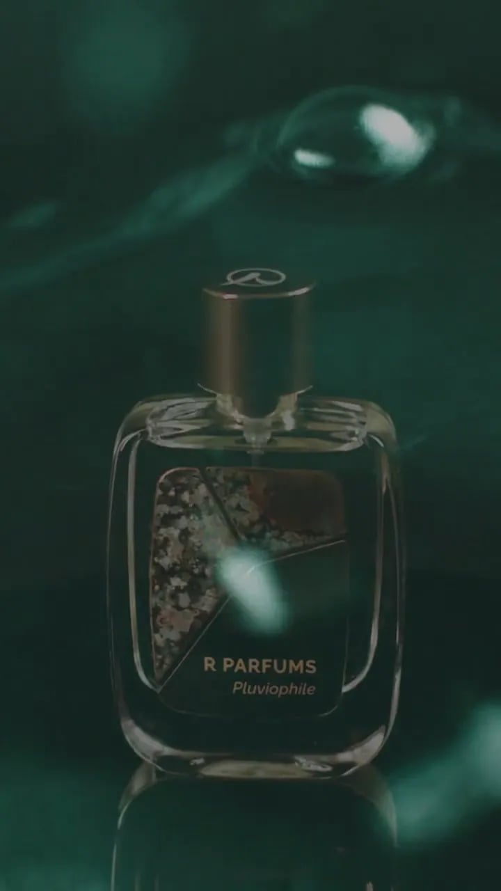 Filem, 2022: Pluviophile dalam botol Patina di atas permukaan hitam yang basah di bawah curahan air, kepingan loyangnya dari dekat, kemudian sebelah tangan mengangkat botol itu. Berulang, tanpa bunyi.